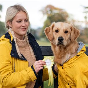 Bark in the Park Dog Show - Woman and her dog in matching yellow coats, sitting on a bench.