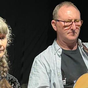Couple playing the guitar and flute against a black background