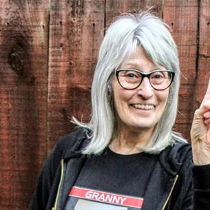 Person wearing glasses doing a peace sign in front of a wooden fence