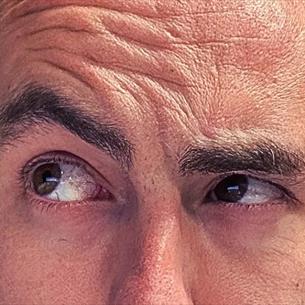 Very close-up of a person's face with quizzical eyebrows on a blue background