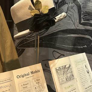 A cream hat with black ribbon on a stand alongside archival Fenwick material