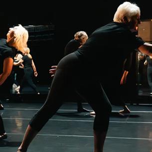 People dancing on a dark stage with low lit lighting.