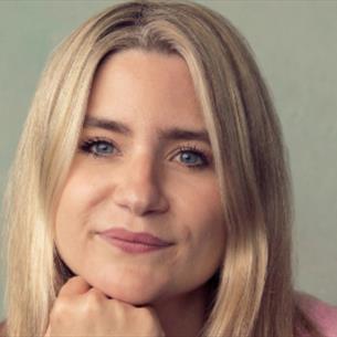 Harriet Kemsley with her chin resting on her hand, smiling with a beige background.