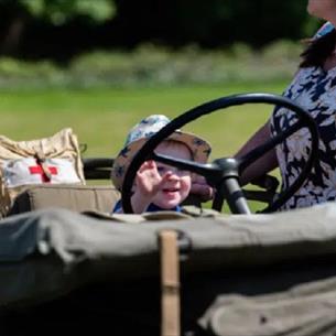 Small child sitting at the wheel of an army truck.
