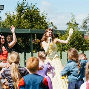Two women dressed as princesses with a crowd of children dancing
