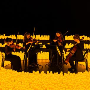 Group of musicians playing string instruments surrounded by hundreds of candles.