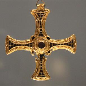A gold cross pendant with arms inlaid with precious stones.