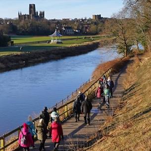 A group walking along the River Wear, with stunning views of the bandstand and Durham Cathedral and Castle.