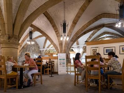 Two families sit at tables in a cafe, which has an arched stone roof.