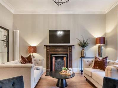 Light coloured living area with a fireplace as a focal point. 2 Large beige sofas place either side of a black coffee table and 2 navy armchairs