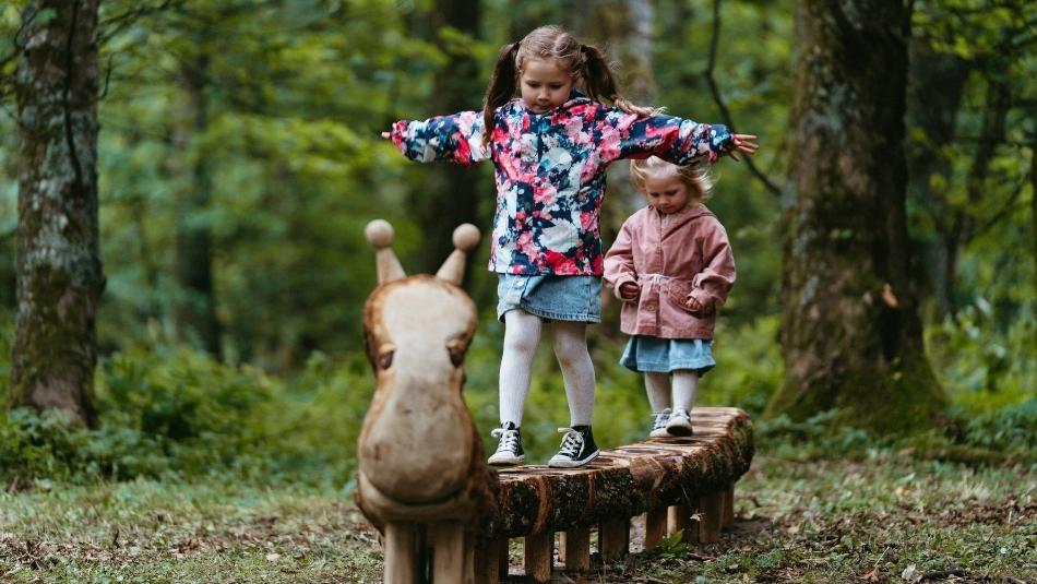 Two children playing on wooden sculpture.