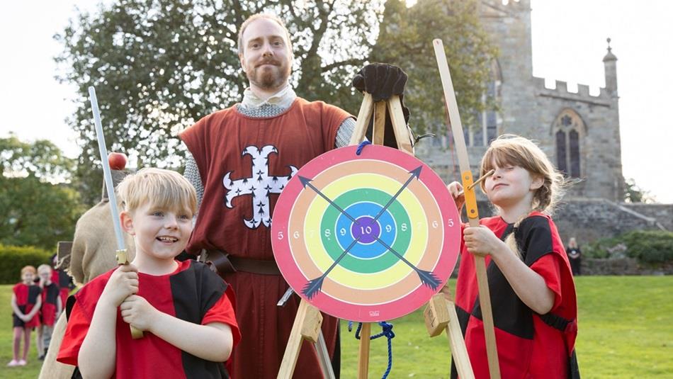 An archery target with two children holding bow and arrows with the instructor