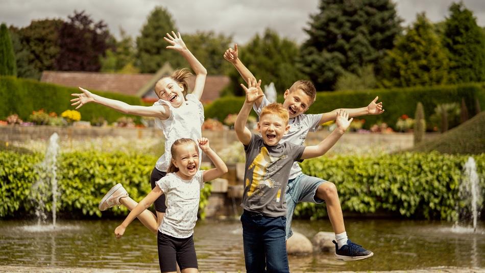 Four children laughing and jumping in the air in front of a pond at Durham University Botanic Garden.