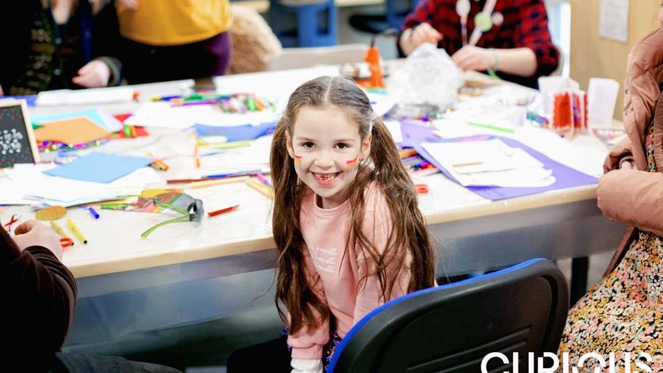 Child with rainbows painted on her face doing arts and crafts