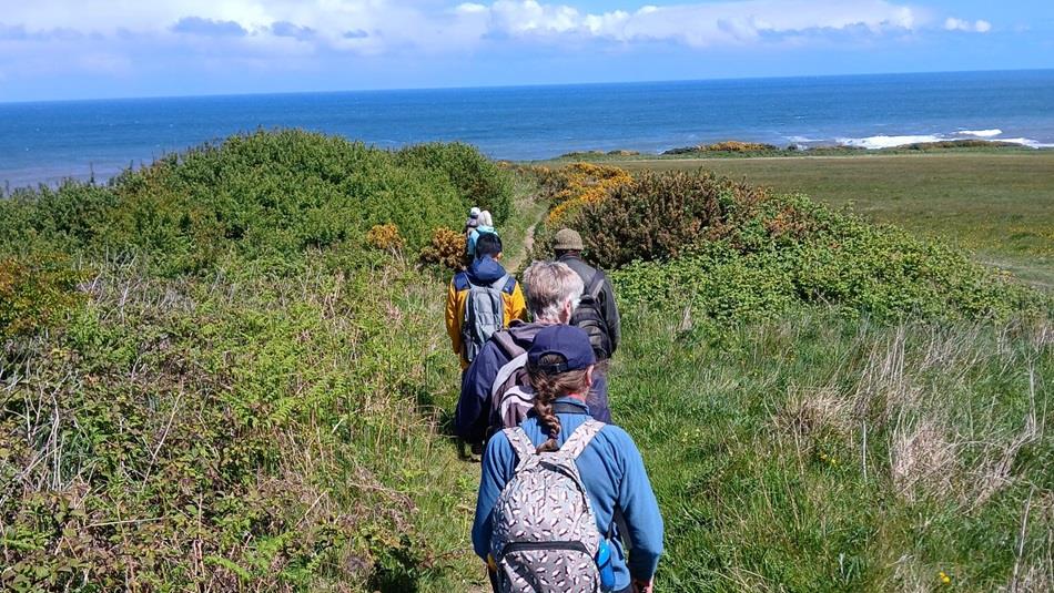 A group of people walking along the Durham Coast on a sunny day, blue sea and blue sky.