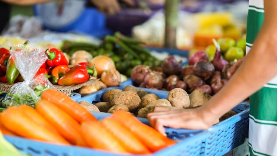 Close up of vegetables at market stall. Person standing next to veg.