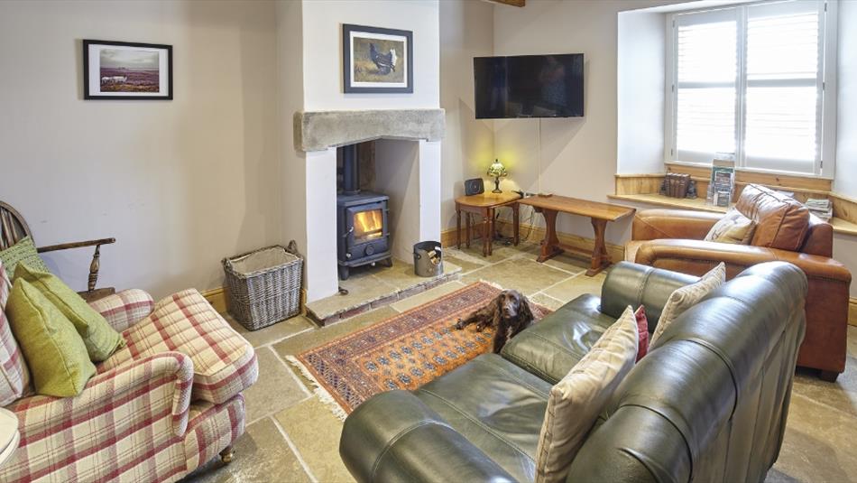 Cosy living are in cottage with real log burner, stone tiled floor and green leather sofa. Wooden beams on the ceiling.