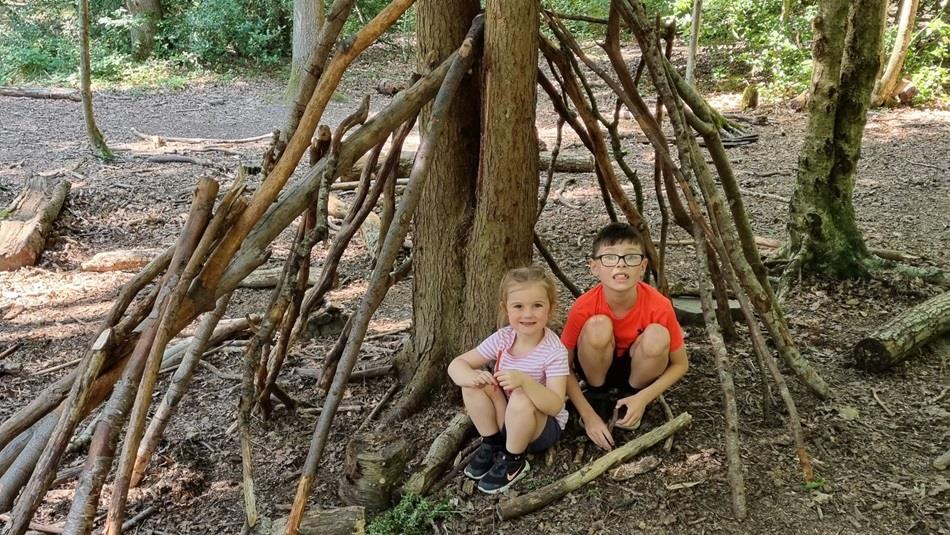 Two children sitting under a den made with twigs and sticks
