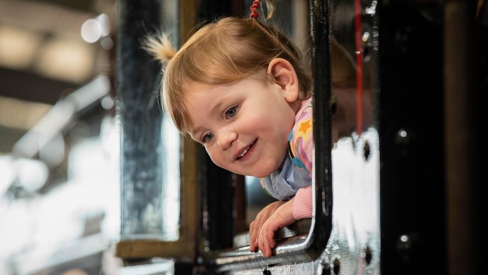 A smiling child peering out of a train window at Locomotion.