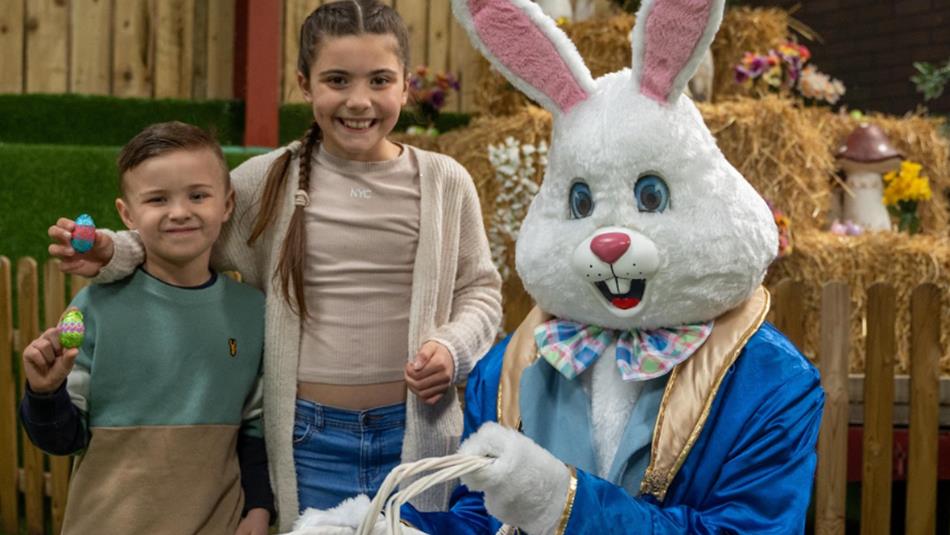 Two children with the Easter Bunny who is carrying a basket full of chocolate eggs.