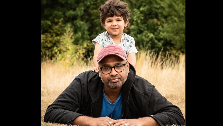 A dad sits on a field with his young son on his shoulders