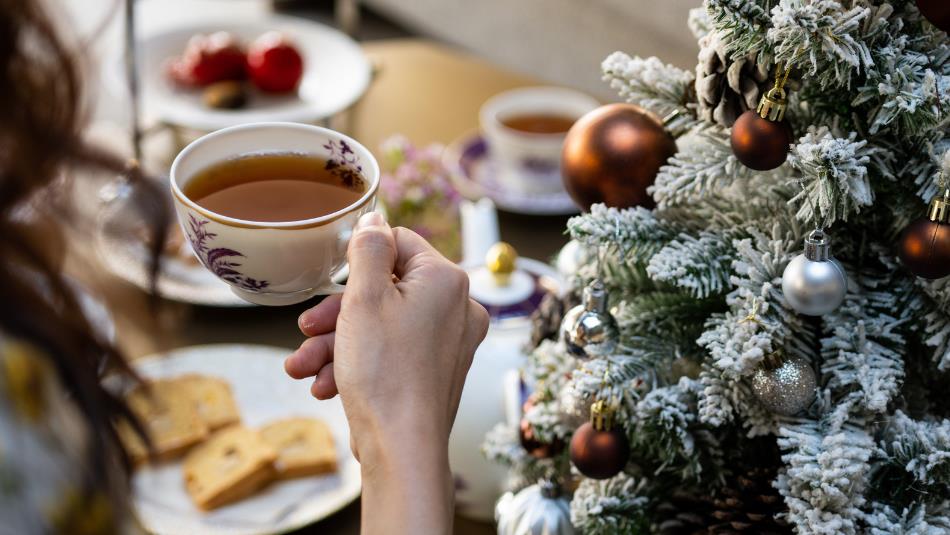 Person drinking tea at Festive Afternoon Tea. Christmas tree on the right.