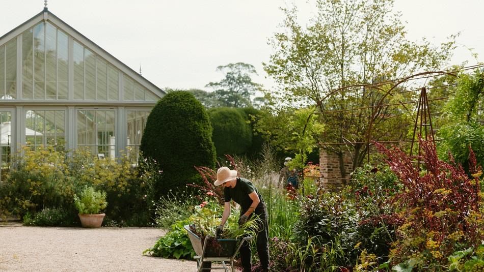 Gardening Through the Seasons with Becky Crowley - Spring.  The greenhouse at Raby Castle with someone filling a wheelbarrow with plants in the foregr