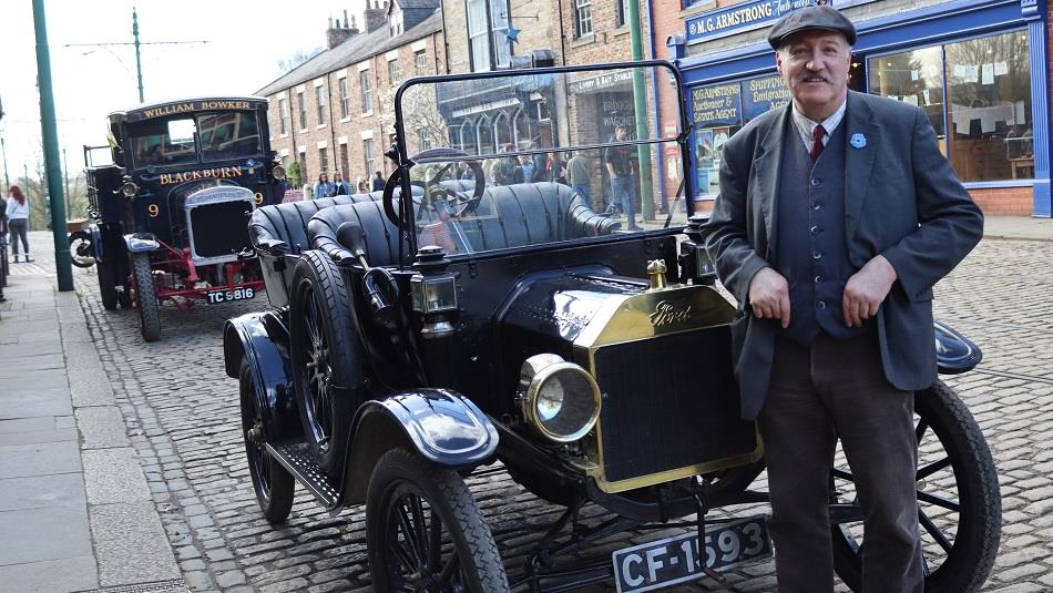 A man in period dress standing beside a vintage car in Beamish Museum's town