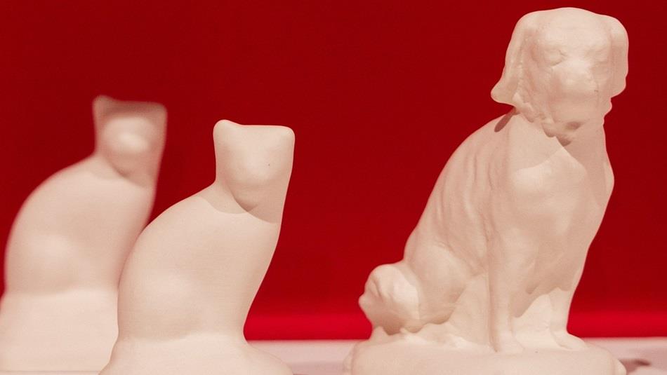 A blank cat and dog bisque figurine on a white shelf with a pink background