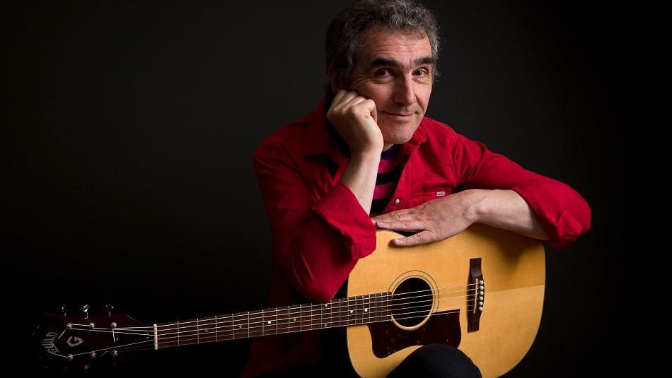 Photo of Jez Lowe wearing a red shirt with a guitar