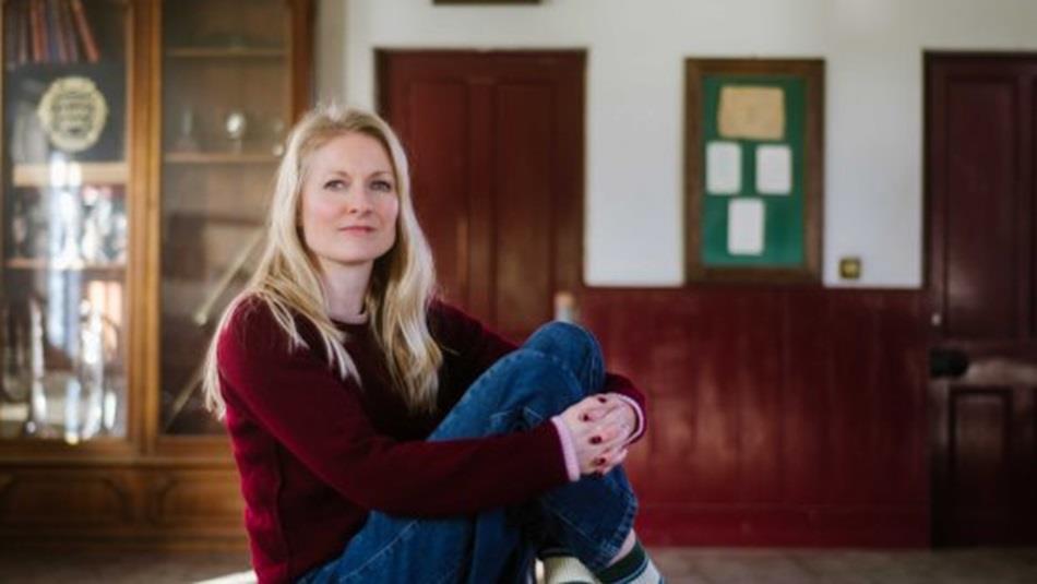 A woman with long blonde hair sitting looking at the camera.