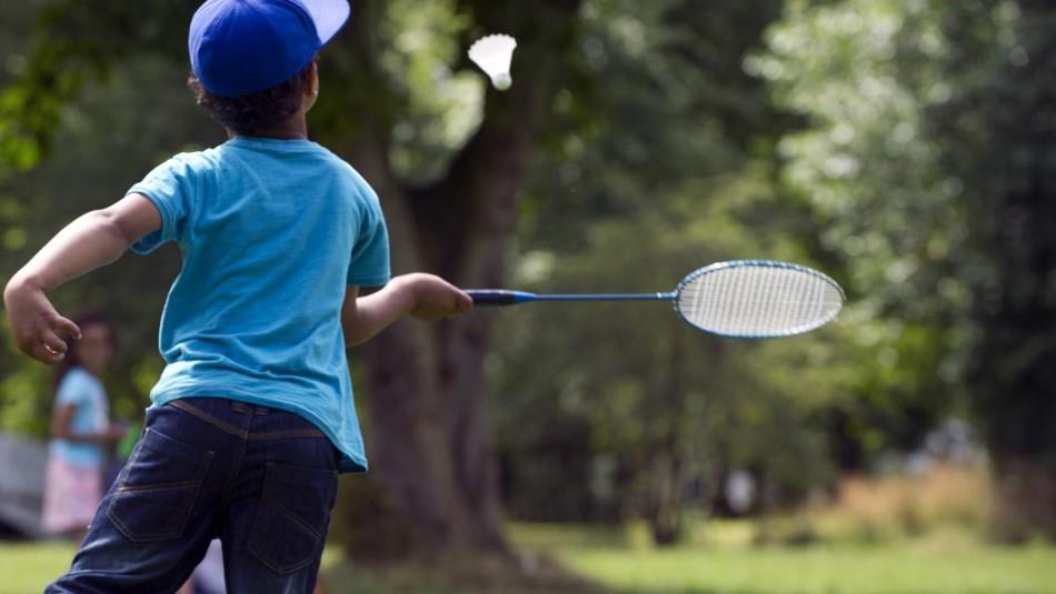 Boy playing badminton. Light blue t-shirt and navy cap.