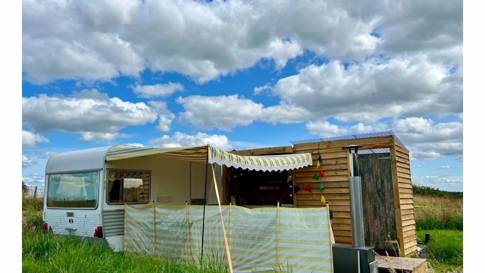 Outside view of vintage caravan with yellow awning, decking area and toilet/shower building