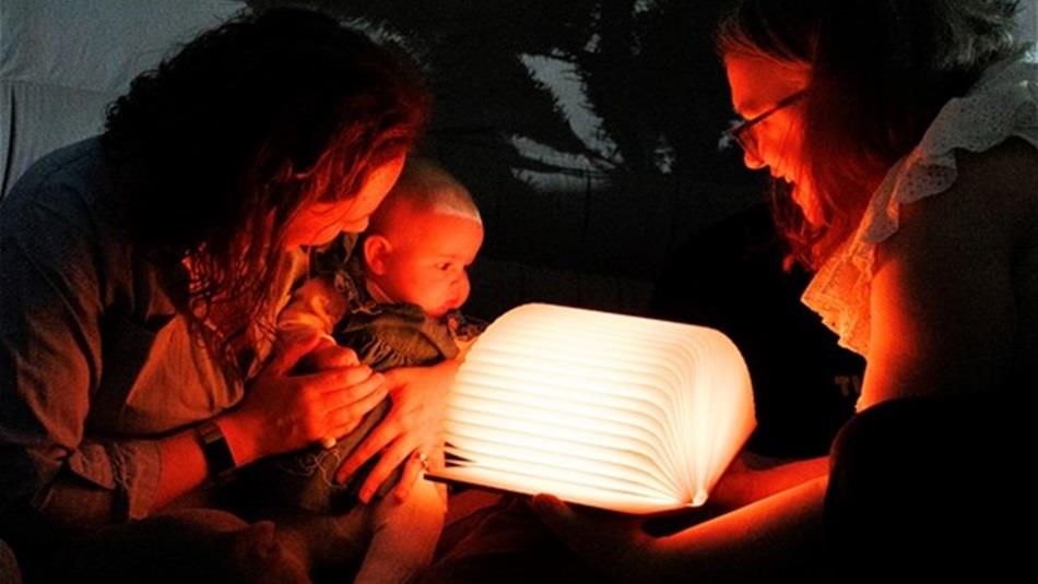 Two adults and a baby looking at an illuminated open book