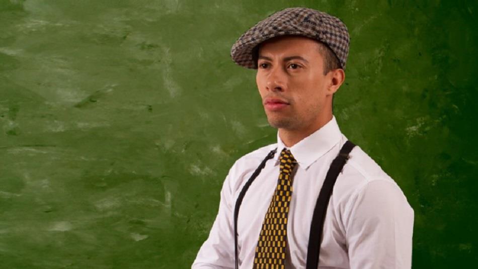 Man wearing a flat cap, white shirt, tie and braces.  Green background.