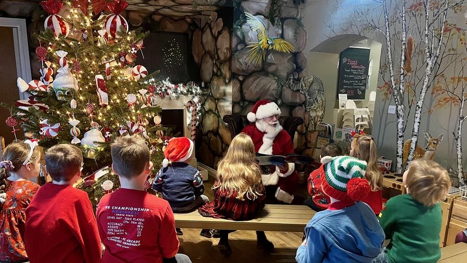 A group of children listening to Santa, telling a story beside a Christmas Tree