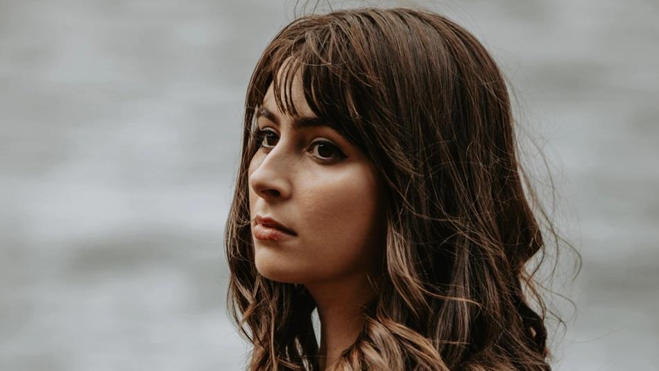 A women with brown hair looking out into the distance, there's a blurred grey background behind her.