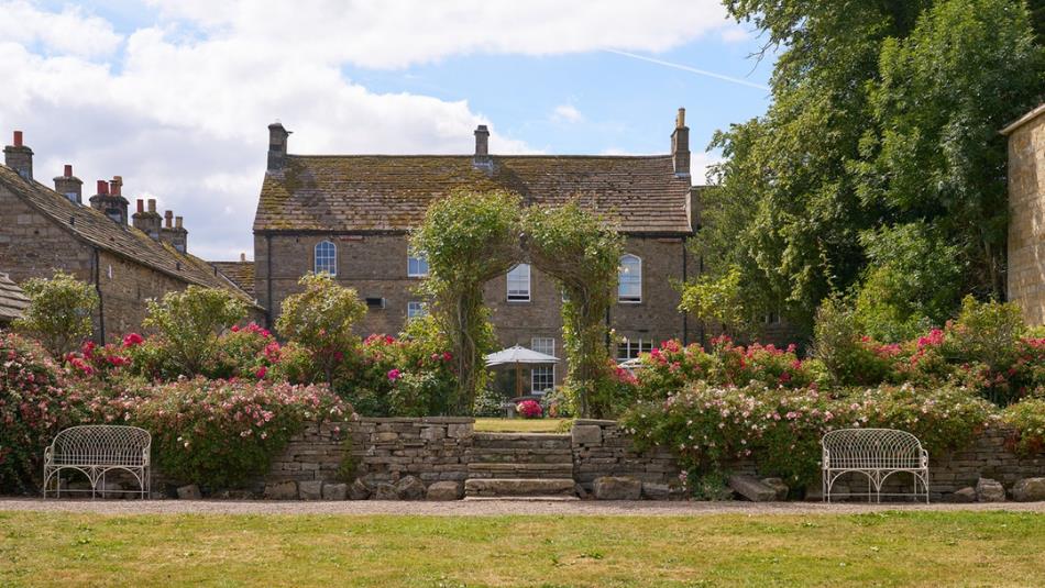 View of the main house at Lord Crewe Arms surrounded by flowers in the garden on a bright sunny day.