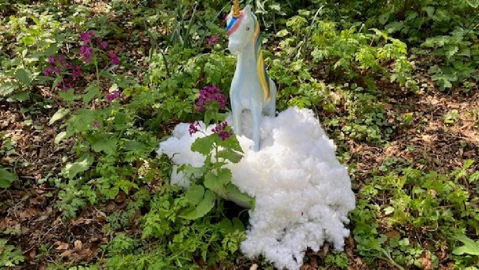 White toy unicorn on vegetation on the ground.