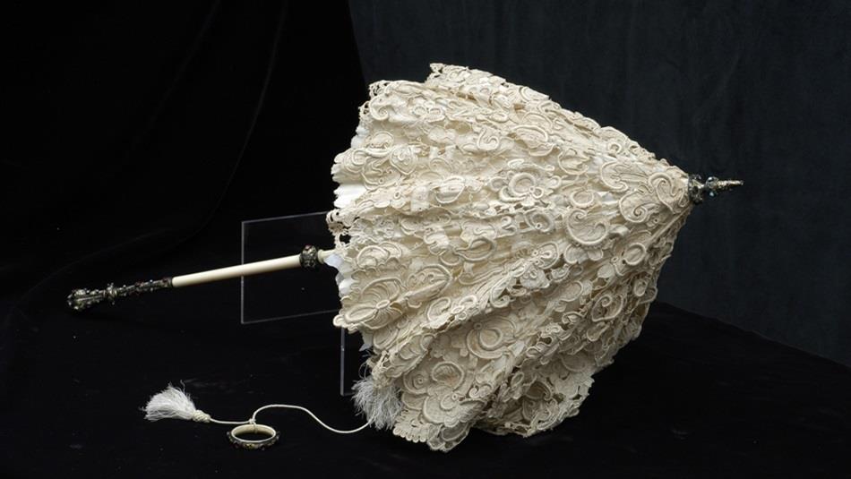An ornate 19th-century lace parasol with an intricately patterned cream lace canopy. The handle is made of ivory or bone with a decorative metal finia