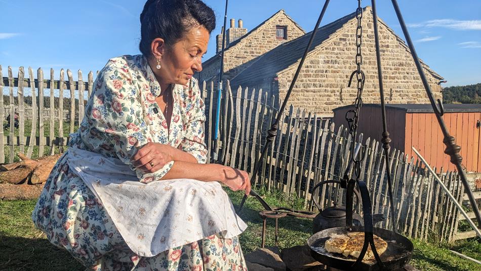 A person is cooking over a fire outdoors, outside Beamish Museum's 1950s Farm