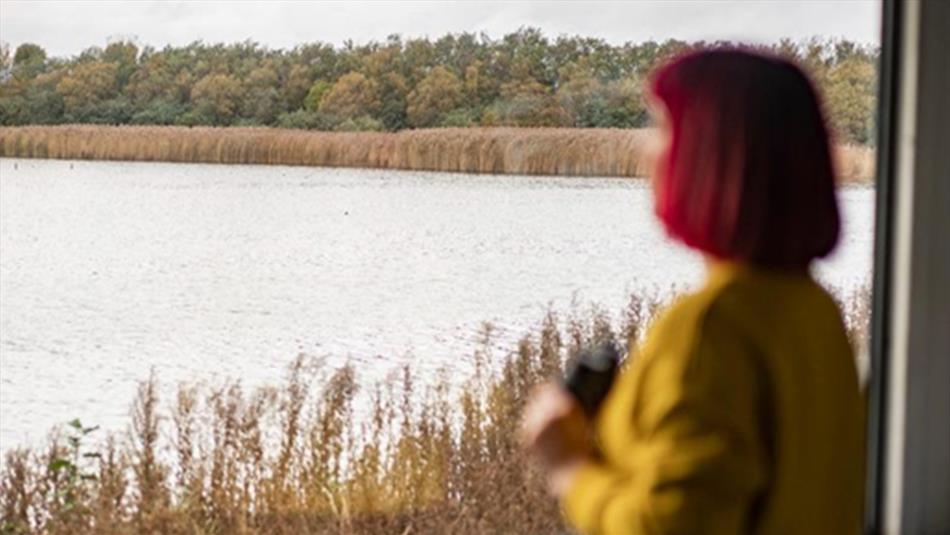 Woman with short red hair, wearing a yellow top, birdwatching with binoculars at RSPB Saltholme. Photo Credit: Brian Morrison (rspb-images.com)