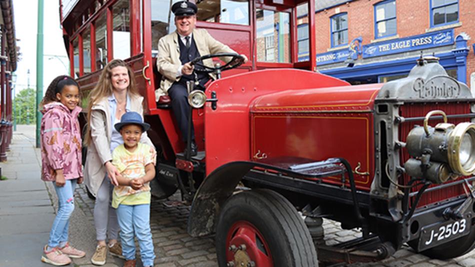 A family posing next to a traditional car at Beamish Museum.