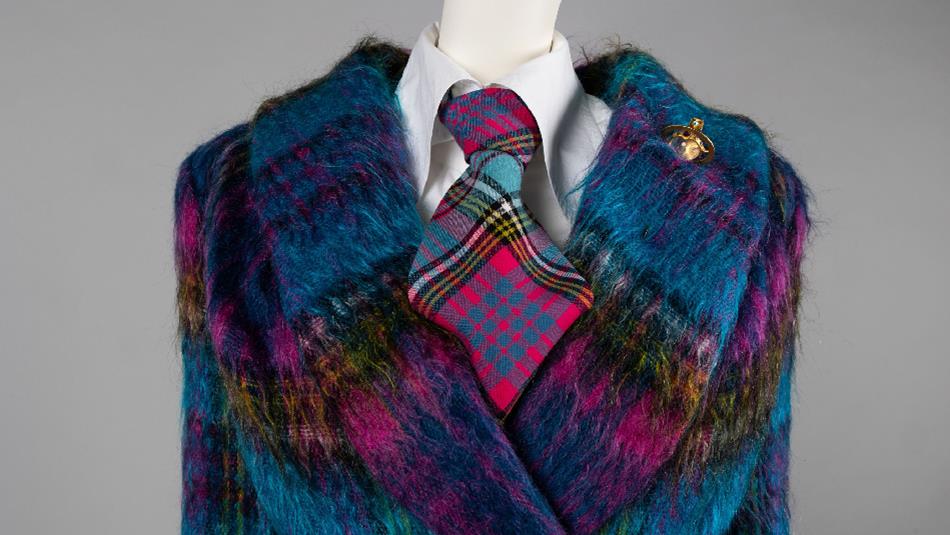 Close-up of a mannequin wearing a vibrant, multicoloured fuzzy coat in shades of blue, purple, and yellow. Underneath is a white shirt with a bold pin