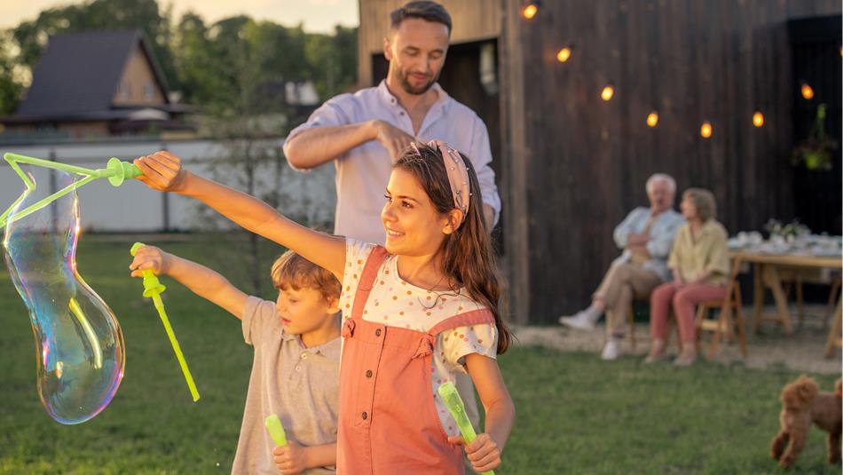 Two children and an adult blowing large bubbles in a fairy lit setting.