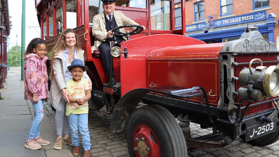 A family at Beamish Museum standing with a vintage bus being driven by a Transport Engager.