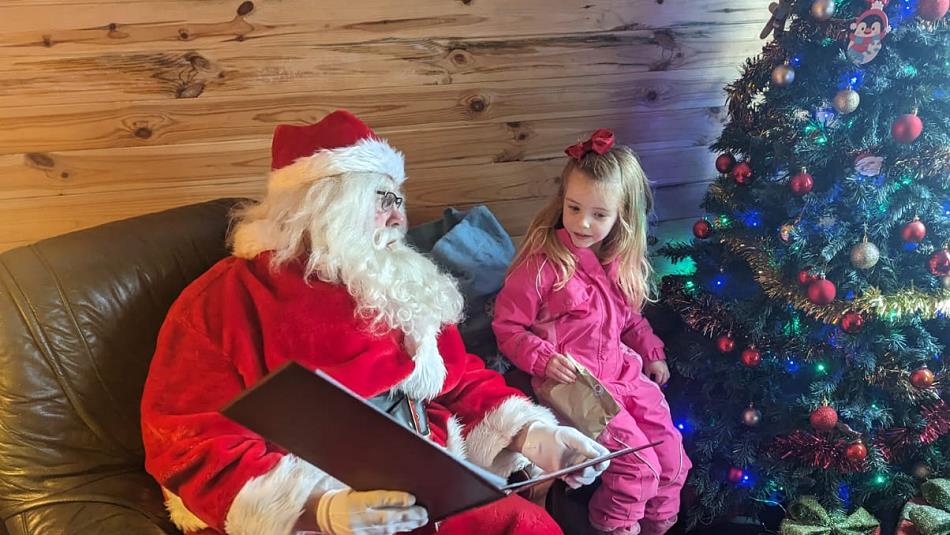 Santa reading to a little girl by a Christmas Tree.