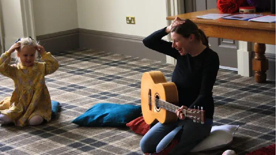 A little girl singing along to a woman playing the guitar.