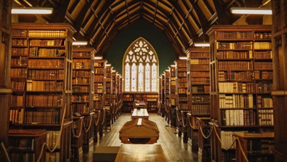 The library at Ushaw Historic House, Chapels and Gardens - rows of historical books and view of arched window at the rear.