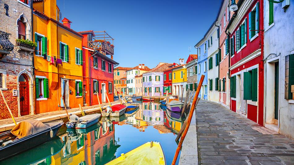 Colourful houses lining a canal with small boats and reflections in the water in Burano, Venice, Italy